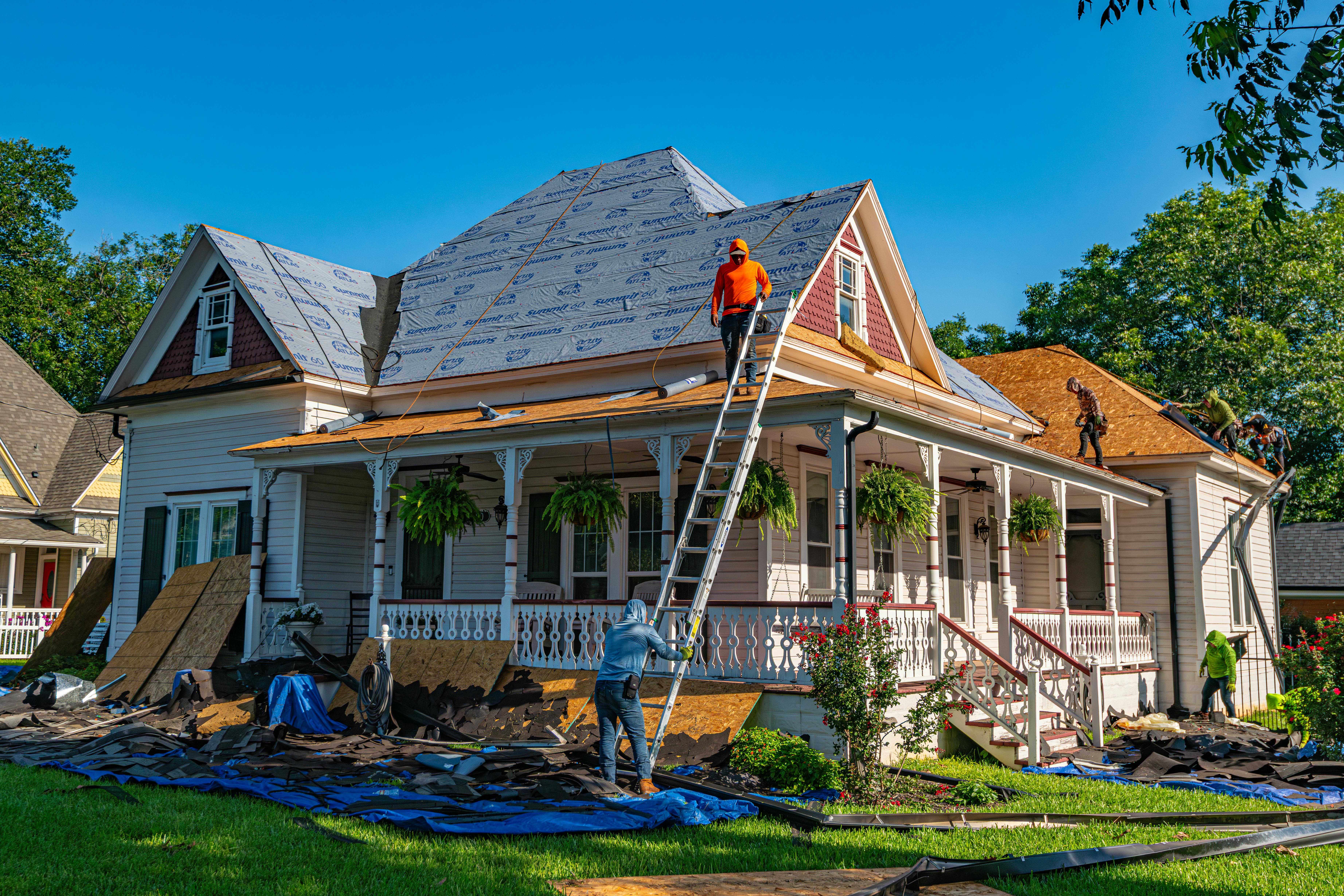 Roof replacement underway on a residential house with ladders and workers visible.